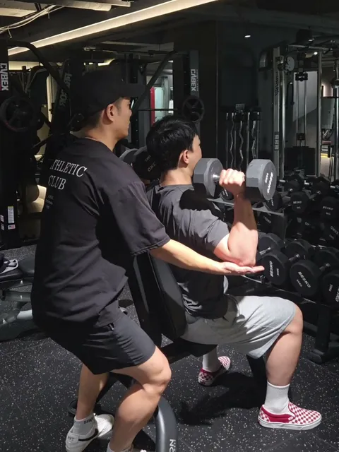 김상현 트레이너가 회원의 덤벨 숄더프레스 자세를 잡아 주는 수업 장면